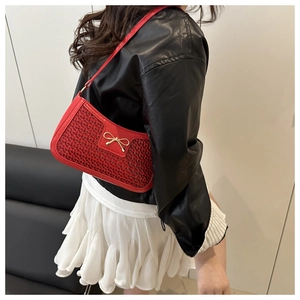 Détail d'un sac porté épaule rouge tressé avec fermoir nœud doré et texture raffinée