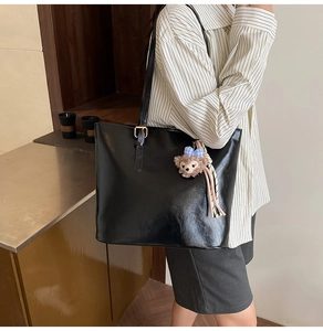 Detail of black faux leather tote bag with gold strap buckle and plush bear charm