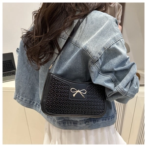 Détail du sac sous l'aisselle noir avec nœud doré et texture tissée sur le modèle