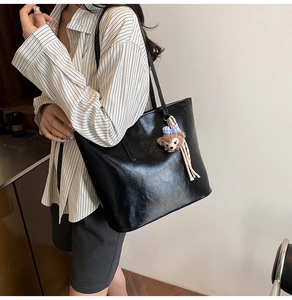 Detail of black glossy faux leather tote bag with shoulder strap and plush charm detail