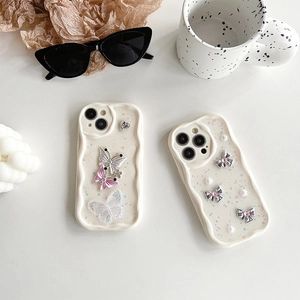 Creamy wave-edge iPhone case with glitter butterfly and pearl accents on a white desk