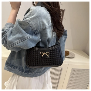 Gros plan d'un sac noir texturé avec boucle nœud dorée et fine bandoulière en cuir