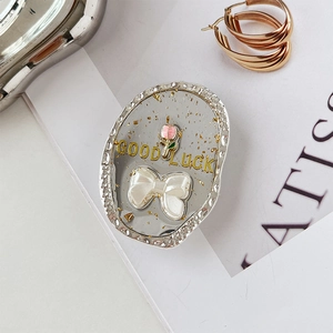Detail eines ovalen Handyhalters mit rosa Blume, weißer Schleife und Good Luck Text