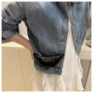 Mini black croissant crossbody bag with gold chain strap shown on a blue denim jacket