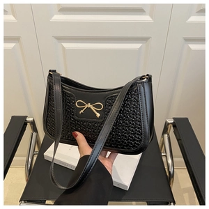 Détail du sac noir à texture tissée avec boucle de nœud doré sur une chaise noire