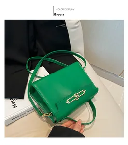 Detail view of a green leather satchel with a golden metal lock on a white cushion