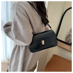 Detail of a chic black shoulder bag with gold metal clasp on a female model