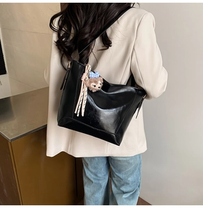 Detail of a black leather tote bag featuring a cute plush bear charm on the shoulder strap