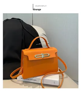 Detail of orange flap crossbody bag with long metal lock and single top handle