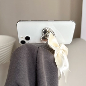 Detail of heart-shaped rhinestone phone grip with a beige satin bow on a smartphone