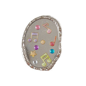 Accessoire notes de musique ovale argenté avec étoiles et strass sur fond gris