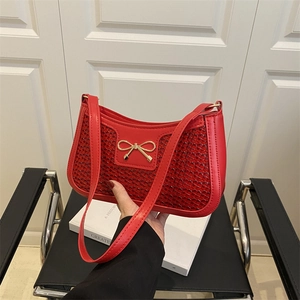 Sac baguette rouge chic avec nœud doré et texture tissée, porté à la main élégamment