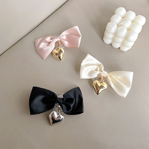 Detailed view of three heart pendant bow hair clips in pink, cream, and black colors