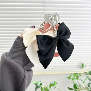 Detail of satin bow phone grip with silver heart ring in black and cream white colors