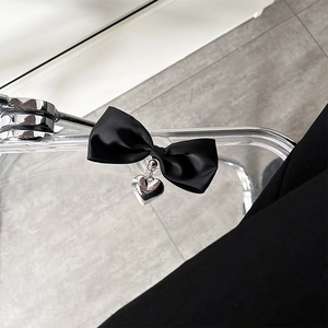 Detail view of black satin bow with silver heart pendant on a modern acrylic surface
