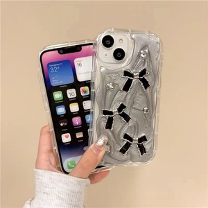 Coque iPhone argentée fluide avec nœuds noirs et strass présentée en main propre