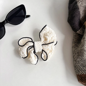 Close-up of white fabric bow phone grip with black piping on elegant flat lay background