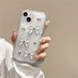 Détail de coque iPhone pailletée avec nœuds 3D et strass vue de main féminine