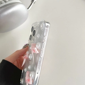Détail de nœuds roses et perles sur coque iPhone transparente avec boutons latéraux précis