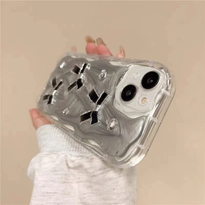 Détail de coque iPhone pailletée avec texture argentée, nœuds noirs et strass brillants