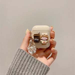 Détail de la coque AirPods crème avec breloque café, figurine fille et pendentif coquillage