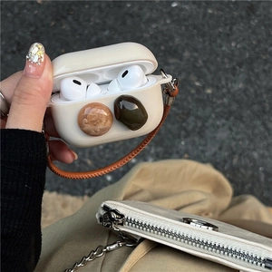 Close-up of beige silicone AirPods case featuring decorative gemstones and a brown wrist strap.