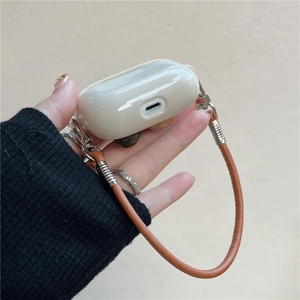 Close-up detail of a cream-colored AirPods Pro case with an elegant brown leather hand strap