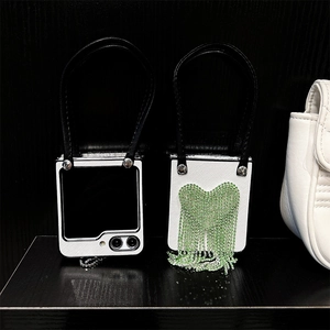 Détail de coque pliante avec cœur en strass vert et lanière à pompon en cuir