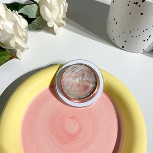 Detailed view of circular crystal phone grip with pink marble texture on a ceramic tray