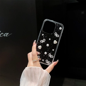 Close-up of clear phone case with black glitter, white bow, pearls and heart charms