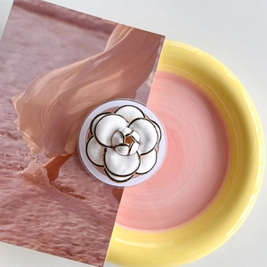 Detail of white camellia magnetic phone grip with golden metal edges on aesthetic plate