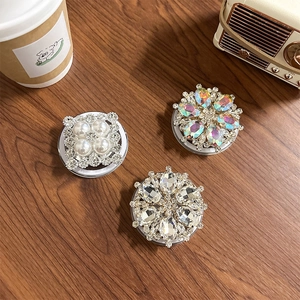 Detail of luxury rhinestone and pearl MagSafe phone grips on a rustic wooden desk