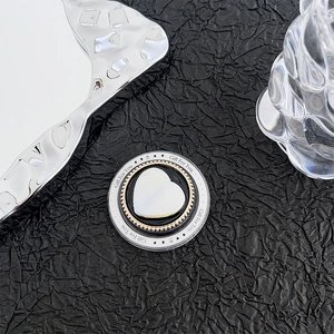 Macro detail of a heart-shaped MagSafe phone grip with gold bead trim on black fabric