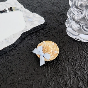 Close-up of a mini straw hat phone grip with blue ribbon and pearls on dark stone