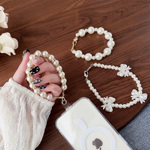 Macro detail of luxury pearl phone lanyards with bow charms on a warm wood surface