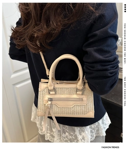 Detail of beige woven mini bag with tassel zipper and leather trim held by a model