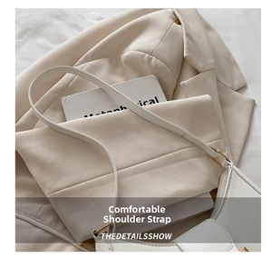 Detail view of the wide leather shoulder strap on a minimalist white underarm handbag