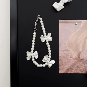 Detailed view of pearl phone strap featuring white bows and a silver lobster clasp