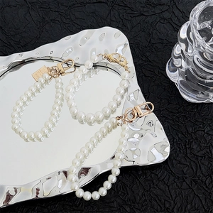 Detailed macro of pearl phone lanyard with gold lobster clasp and square charm