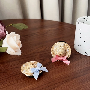 Detail of a straw hat phone grip with a pink bow and pearl accents on a wooden desk