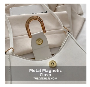 Detail of white leather dumpling bag with gold U-shaped handle and magnetic clasp