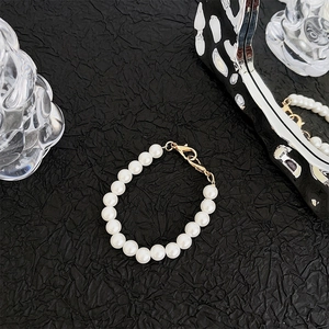 Detail of white pearl phone lanyard with gold lobster clasp on black textured background
