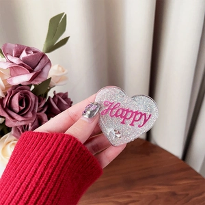 Macro detail of heart-shaped glitter phone grip featuring pink Happy text design