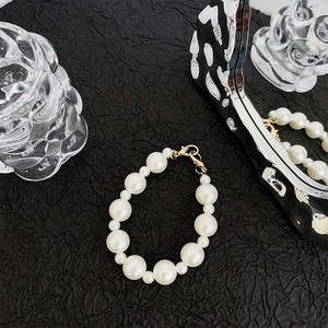 Detail of luxury pearl phone strap with golden lobster clasp on textured black backdrop