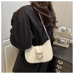 Close-up of beige leather shoulder bag featuring a large gold horseshoe metal buckle