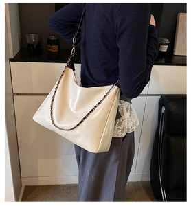 Detail of glossy cream hobo bag with metal chain and leather shoulder strap