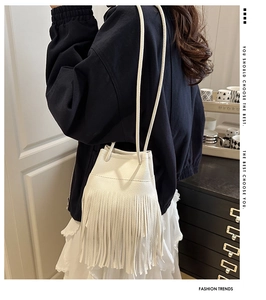 Detail of white faux leather bucket bag featuring long fringe tassels and drawstring closure
