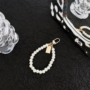 Detail of pearl wrist strap with golden clasp and a miniature gold bar pendant charm