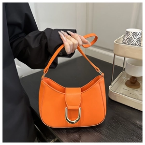 Close-up of bright orange crescent bag featuring a prominent golden horseshoe buckle