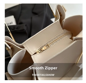Close-up of smooth gold zipper closure and textured beige leather on minimalist handbag